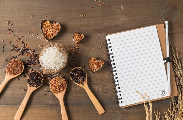 arroz variado: Baya de arroz, arroz mezclado rojo marrón y tailandés con el cuaderno en blanco en centrico de madera marrón