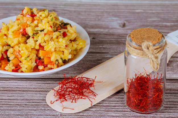 Arroz con verduras con azafrán en una placa blanca sobre un fondo de madera