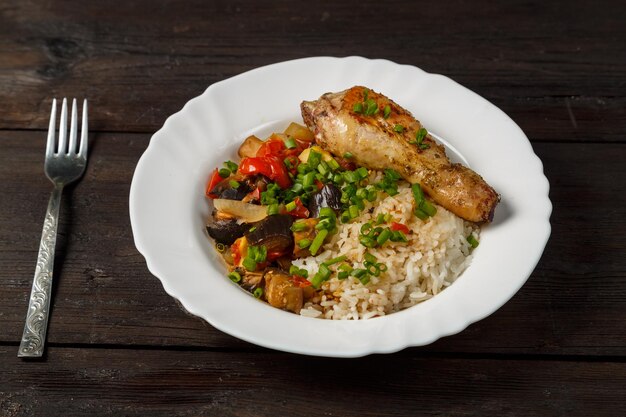 Arroz con verduras guisadas en salsa y pierna de pollo en un plato blanco sobre una mesa de madera