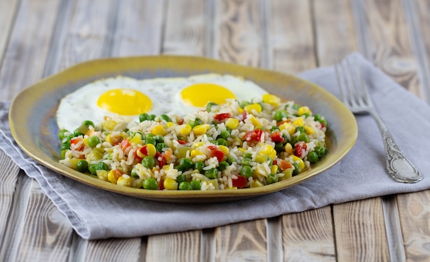 Arroz con verduras pimienta, guisantes, maíz y huevos fritos en un plato