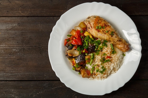 Arroz con verduras en salsa y muslo de pollo en un plato blanco sobre una mesa de madera