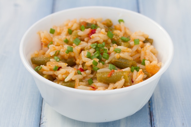 Arroz con verduras en un tazón blanco sobre madera azul