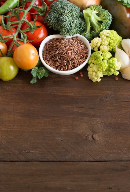 Arroz vermelho cru em uma tigela com legumes na madeira