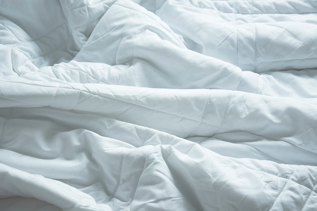 Foto arrugue la manta sucia en el dormitorio después de despertarse por la mañana, de dormir en una noche larga, detalles de edredón y manta, una cama sin hacer en la habitación del hotel con una manta blanca.