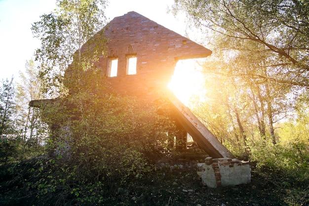 Arruina el viejo bosque de la casa de ladrillo en ruinas contra el sol brillante