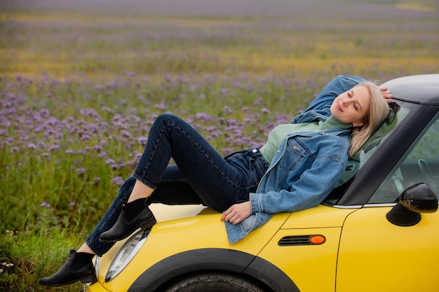 Art blonde Frau mit einem Auto nahe Blumen in der Herbstzeit abgelegt