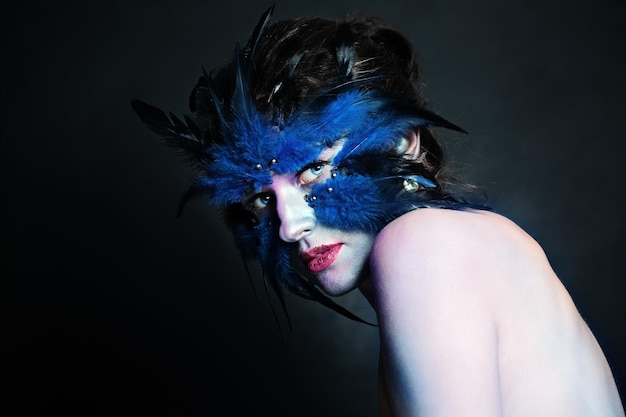 Arte creativo personaje de Halloween Mujer modelo perfecta con plumas negras y azules maquillaje de pájaro
