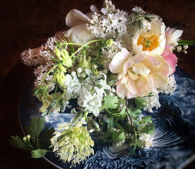 Arte de organizar buquês de flores Buquê romântico em um prato decorativo e em um fundo escuro Na composição tulipas allium espinheiro aquilegia e lilás