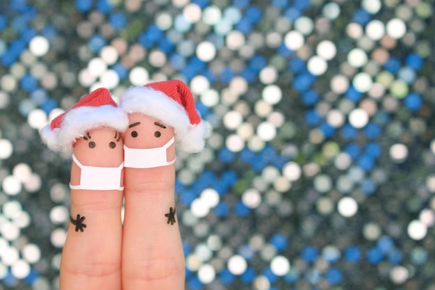 El arte de los dedos de la pareja en la máscara médica de COVID-2019 celebra la Navidad. Concepto de personas con sombreros de año nuevo.