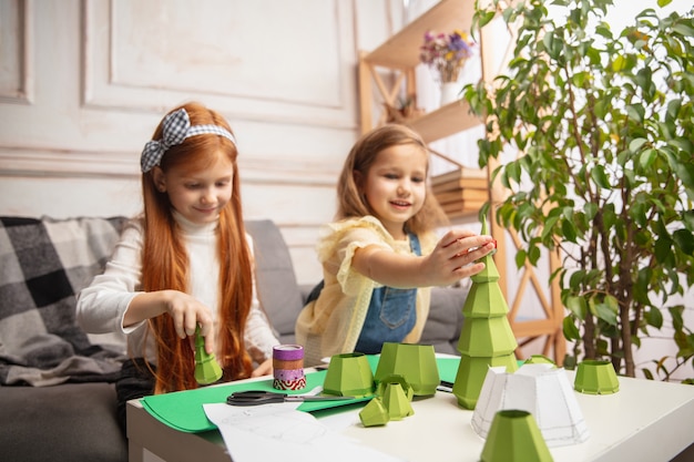 Arte. Duas crianças pequenas, meninas juntas na criatividade da casa. Crianças felizes fazem brinquedos artesanais para jogos ou comemoração de ano novo. Pequenos modelos caucasianos. Infância feliz, preparação para o Natal.
