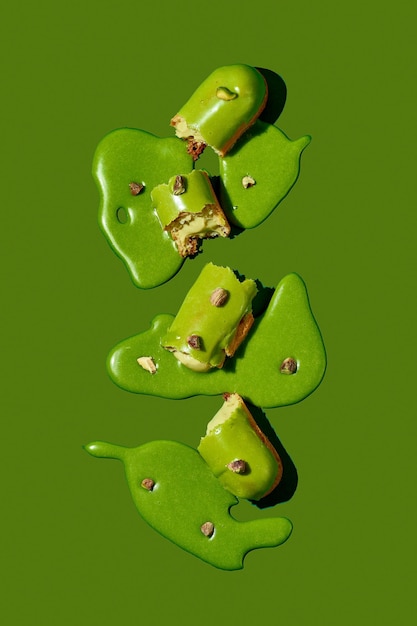 Arte con un eclair Eclair roto en charcos de guinda sobre fondo verde Cartel conceptual de comida monocromática para profiteroles de pistacho