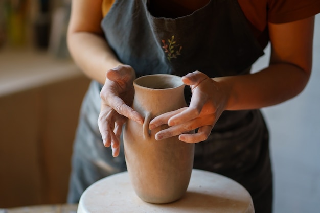 Foto arte hobby mujer en delantal trabajar con arcilla moldeando jarra de cerámica en el estudio creativo durante la clase magistral