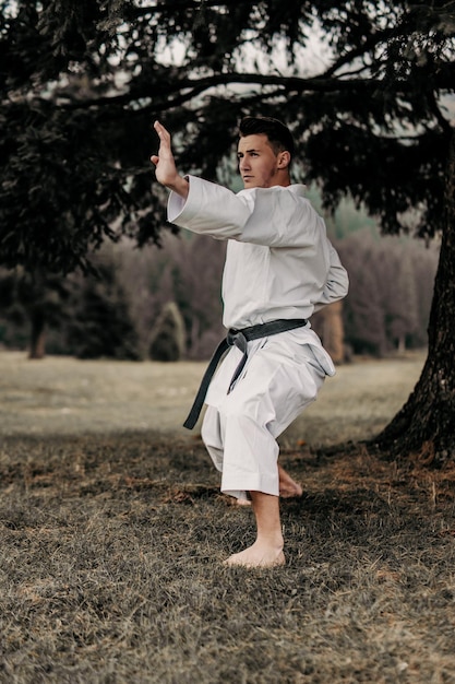 Foto arte marcial de karate un hombre en un kimono con cinturón negro entrena en el espacio libre de la montaña