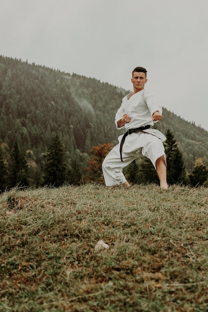 Arte marcial de karate un hombre en un kimono con cinturón negro entrena en el espacio libre de la montaña