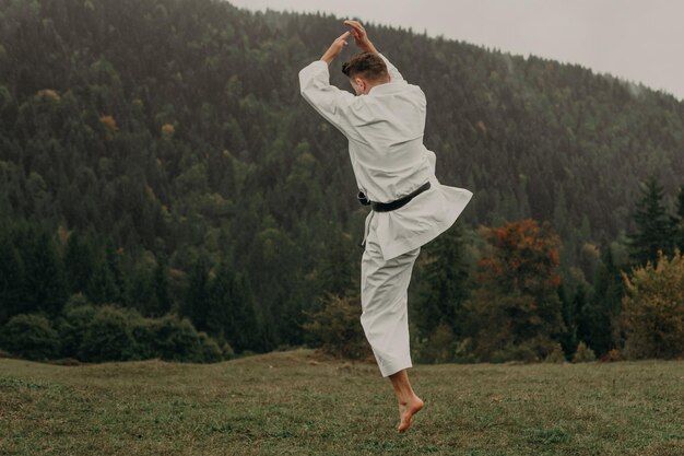 Foto arte marcial de karate un hombre en un kimono con cinturón negro entrena en el espacio libre de la montaña