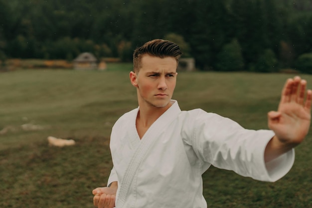 Arte marcial de karate un hombre en un kimono con cinturón negro entrena en el espacio libre de la montaña