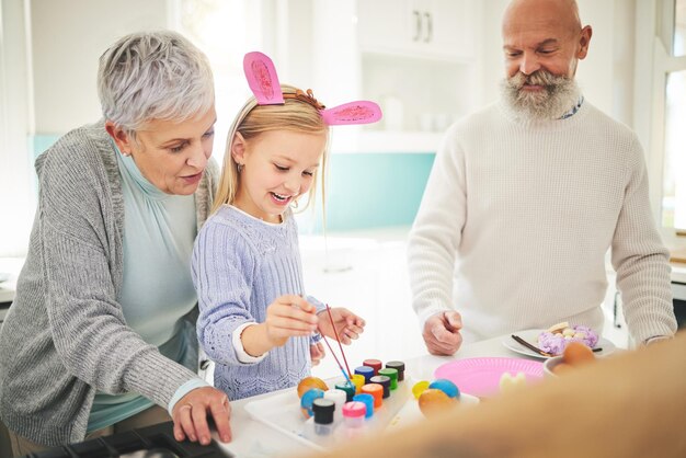 Arte de Pascua y una niña pintando con sus abuelos en su casa por amor o celebración juntos Cocina familiar o huevo con una pareja mayor y su nieto en una casa para pintar