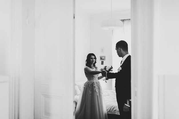 Arte, ruído, grão. A primeira reunião dos noivos em casa, vista pela porta. O noivo leva a noiva pela mão. Foto preto e branco. Manhã de casamento.