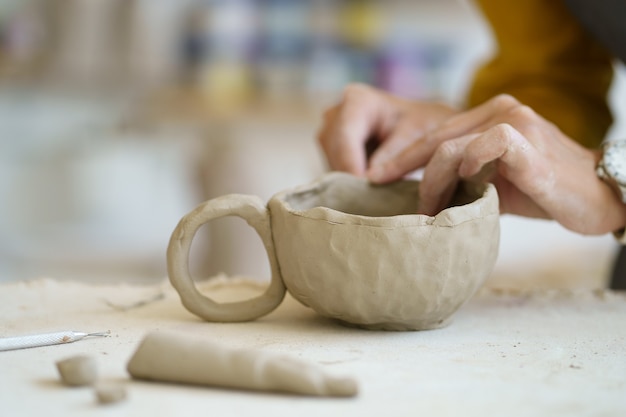 Arte-terapia na aula de cerâmica mãos femininas moldando o trabalho do artista de copos de oleiro com argila crua em estúdio