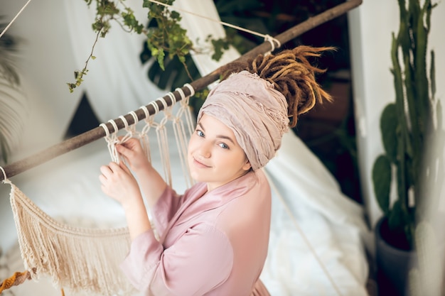 Artesanía. Mujer joven en un sombrero tejiendo macramé y mirando positivo