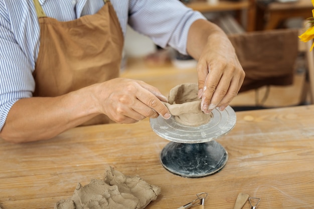 Artesano en delantal. Artesano profesional creativo vistiendo delantal marrón trabajando con torno de alfarería