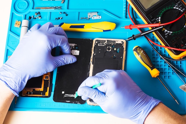 Artesano con guantes de goma repara o da servicio a un teléfono móvil en una alfombrilla de goma especial para reparar la vista desde el interior