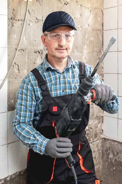 El artesano con ropa de trabajo y gafas protectoras sostiene un perforador en sus manos.
