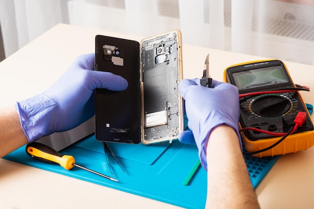 Artesão em luvas de borracha reparam ou fazem a manutenção de um telefone celular em um tapete de borracha especial para reparo de dentro