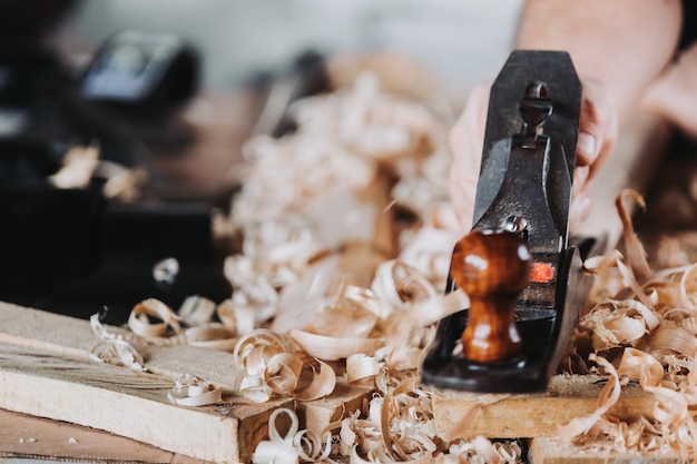 Artesão irreconhecível usando escova de carpinteiro de aço velho esculpindo uma vara de madeira, em sua oficina.