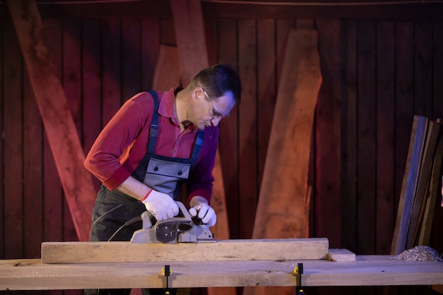 Artesão masculino de meia idade trata peça de madeira com plaina elétrica