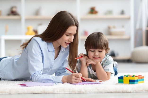 Arteterapia para crianças jovem professora desenhando com garotinho bonitinho interessado assistindo a