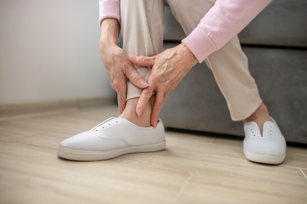 Arthritis. Nahaufnahmebild der Hände der Frau, die ihr Bein berühren