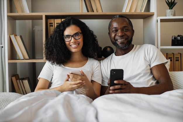 Artículo de lectura familiar multirracial sobre teléfonos inteligentes en la cama