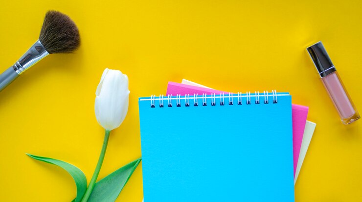 Foto artículos de maquillaje y cuadernos junto a un tulipán