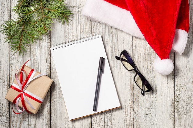 Artículos de Navidad y de negocios con espacio de copia recortada Gorra de Santa Bloc de notas Bolígrafo Gafas y caja de regalo decorada y abeto