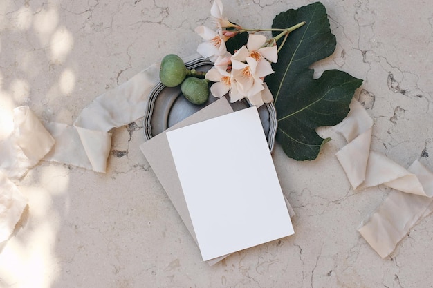 Artigos de papelaria de casamento de marca de verão Design mediterrâneo Convite de cartão de felicitações simulado em placa de prata vintage Folhas de figo e flores de oleandro Fundo de mármore bege Vista superior plana