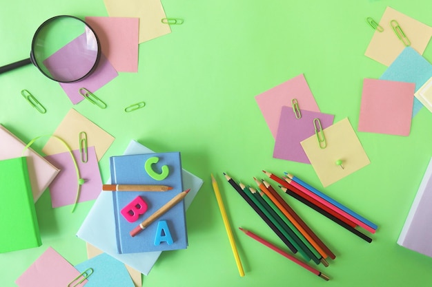 Artigos de papelaria e um papel de cor pastel de despertador em uma vista superior de fundo verde