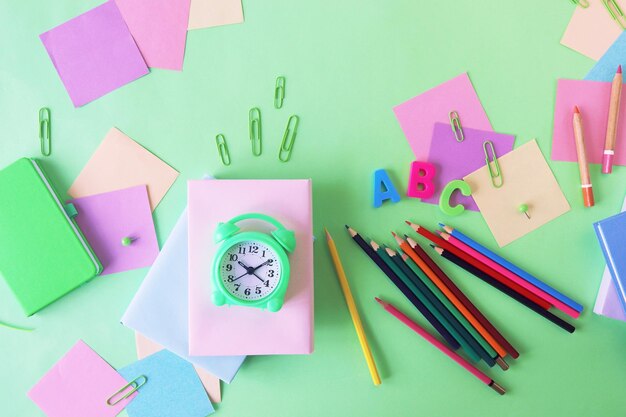 Artigos de papelaria e um papel de cor pastel de despertador em uma vista superior de fundo verde