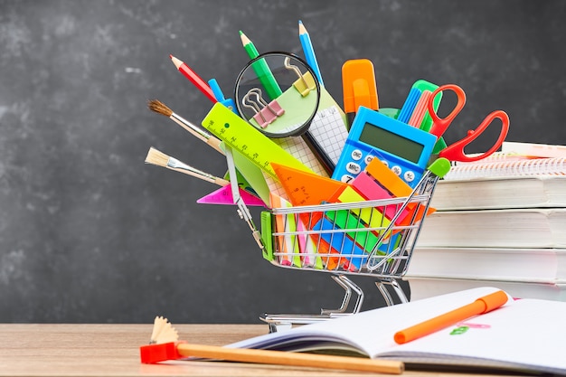 Artigos de papelaria para escola em um carrinho no fundo de um quadro negro