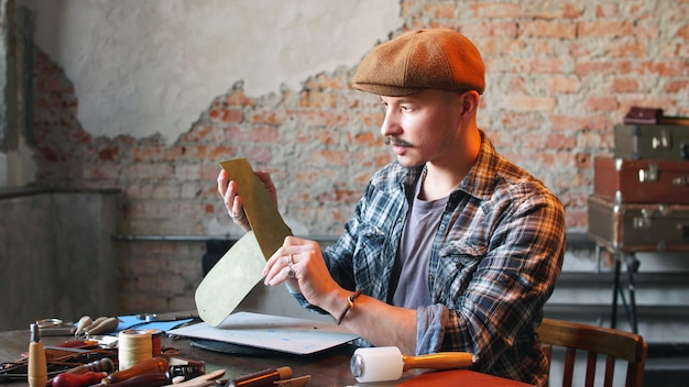 Artisan in seiner Werkstatt stellt eine Lederbrieftasche her. Das Konzept der handwerklichen Herstellung von handgefertigten Echtlederprodukten