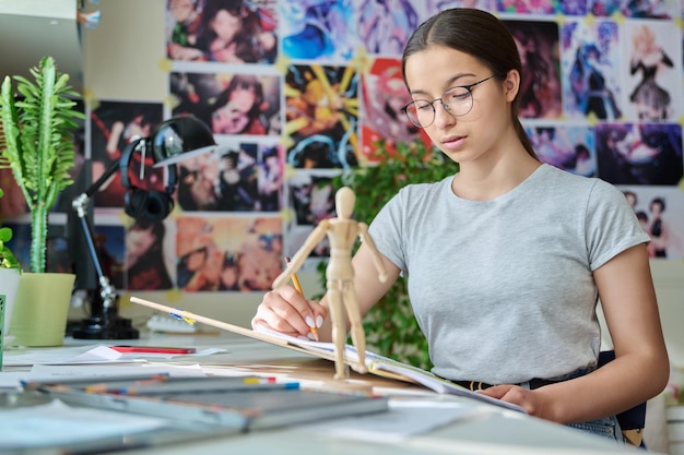 Foto artista adolescente creativa dibujando con un lápiz sentada en la mesa en casa usando un maniquí de madera creatividad escuela afición ocio estilo de vida adolescencia concepto juvenil