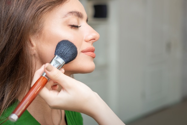 Artista aplicando maquiagem profissional de base tonal no rosto de uma bela jovem caucasiana na sala de maquiagem. base para maquiagem.