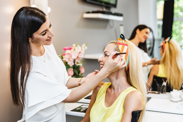 Artista aplicando maquiagem profissional de bela mulher loira de meia-idade.