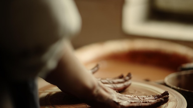 Foto artista de arcilla no reconocida poniendo las manos en la rueda del alfarero en el estudio dama terminando el proceso de artesanía en la cerámica closeup mano de mujer desconocida descansando en el taller