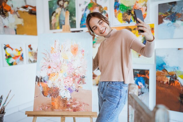 Artista asiática tomando fotografías de su propia pintura con smartphone