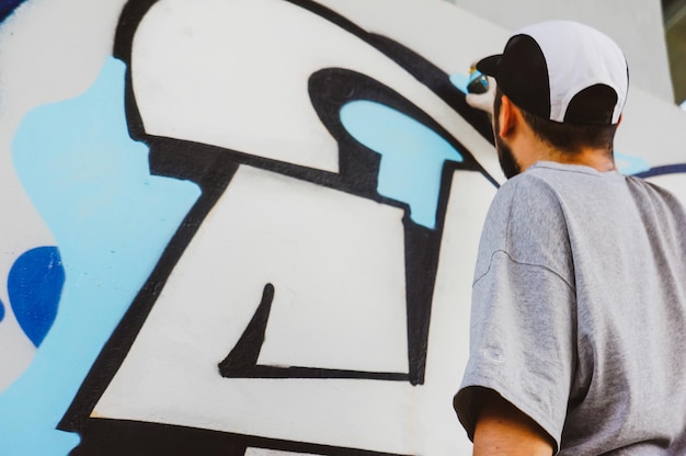 Artista callejero dibuja grafitis coloridos y vibrantes El concepto de arte moderno con un artista urbano aplica grafitis brillantes en la pared gris