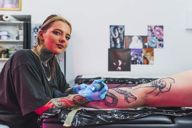 Artista caucásica tatuada durante el proceso de tatuar a su cliente guantes protectores y