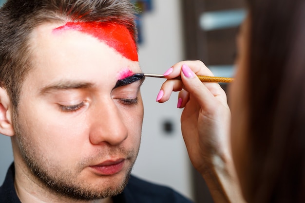 Artista chica pinta en la cara de un hombre