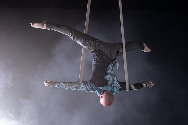 Artista de circo en las correas aéreas con traje en el negro y ahumado.