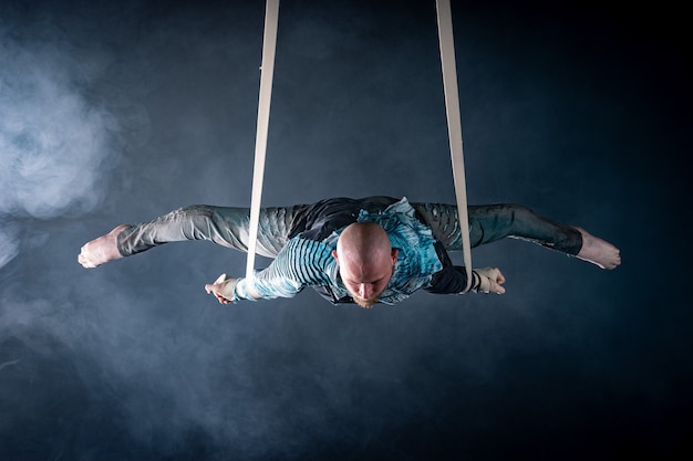 Artista de circo en las correas aéreas con traje en el negro y ahumado.